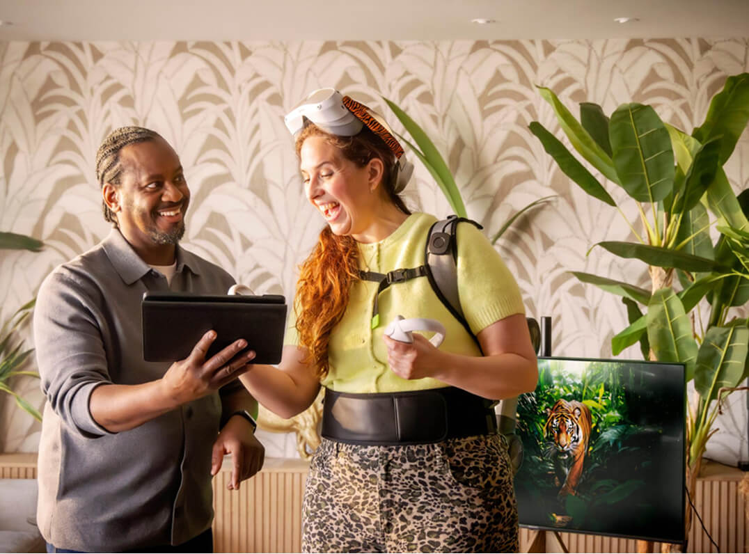 Man en vrouw lachen terwijl ze samen naar een tablet kijken; de vrouw draagt VR-apparatuur.