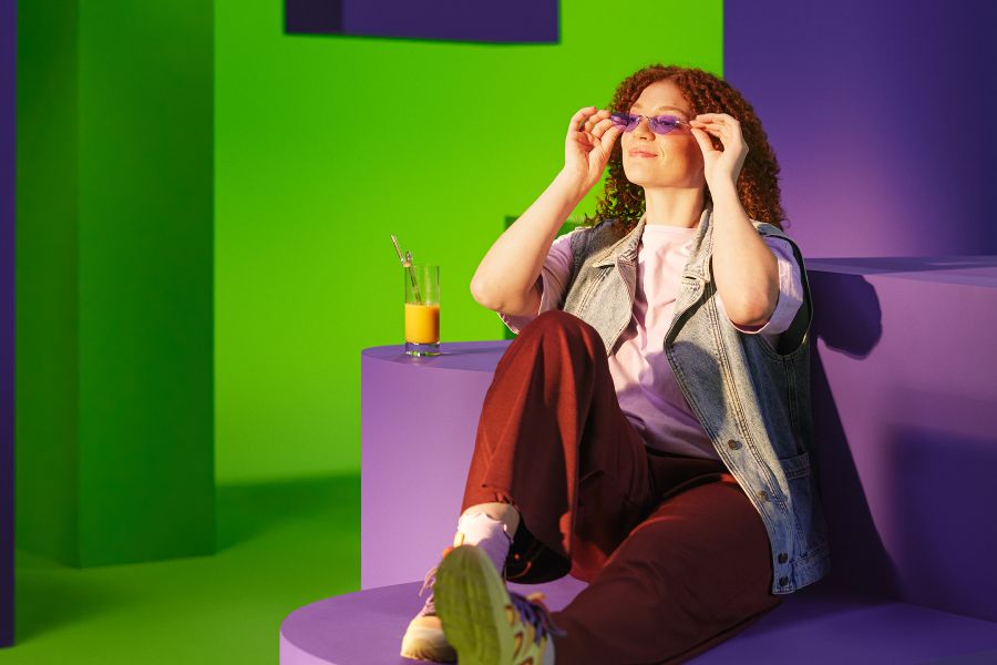 Vrouw zit op een paarse bank met een zonnebril op